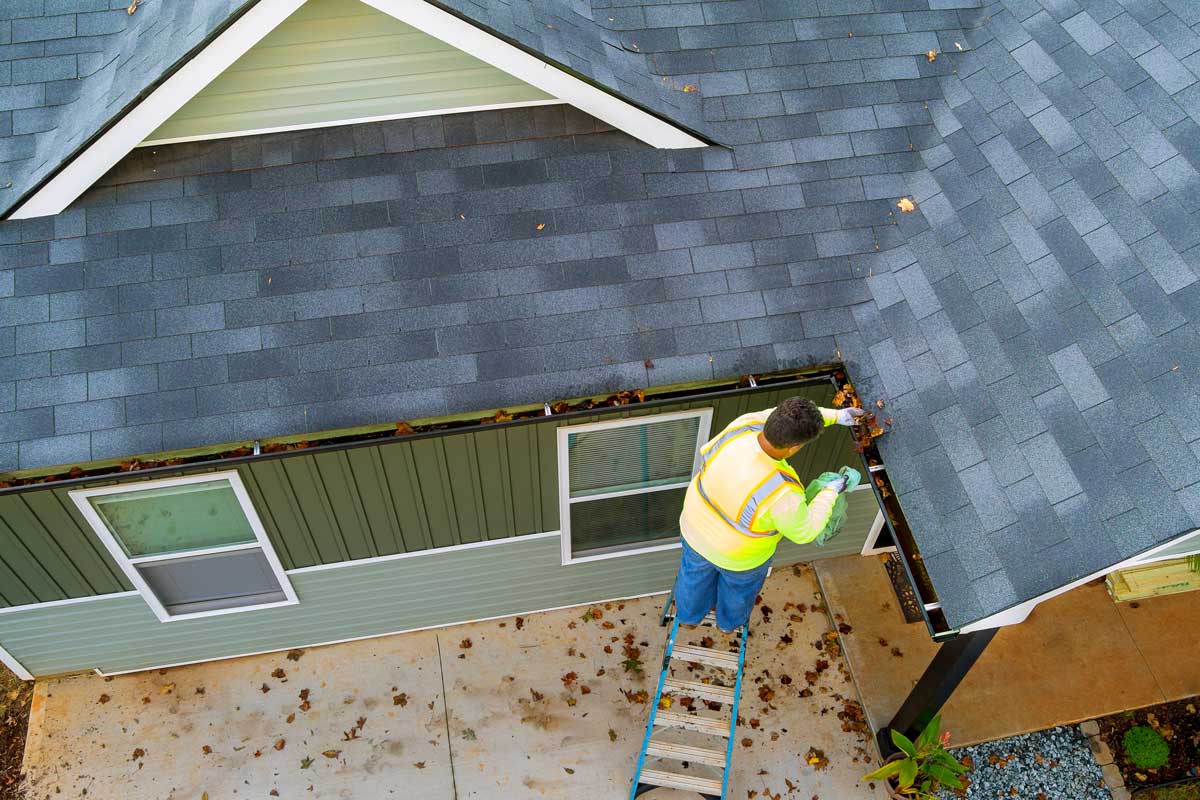 A person on a ladder cleaning gutters on a roof.